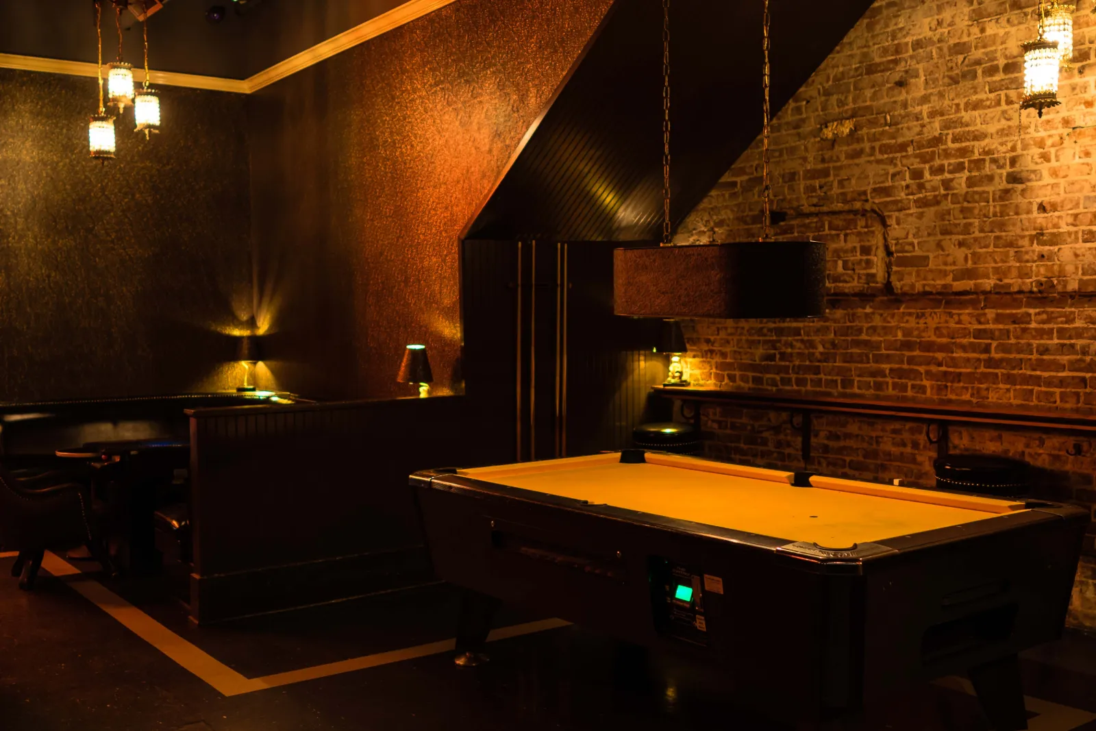 The pool table under its hanging lamp, brick wall behind