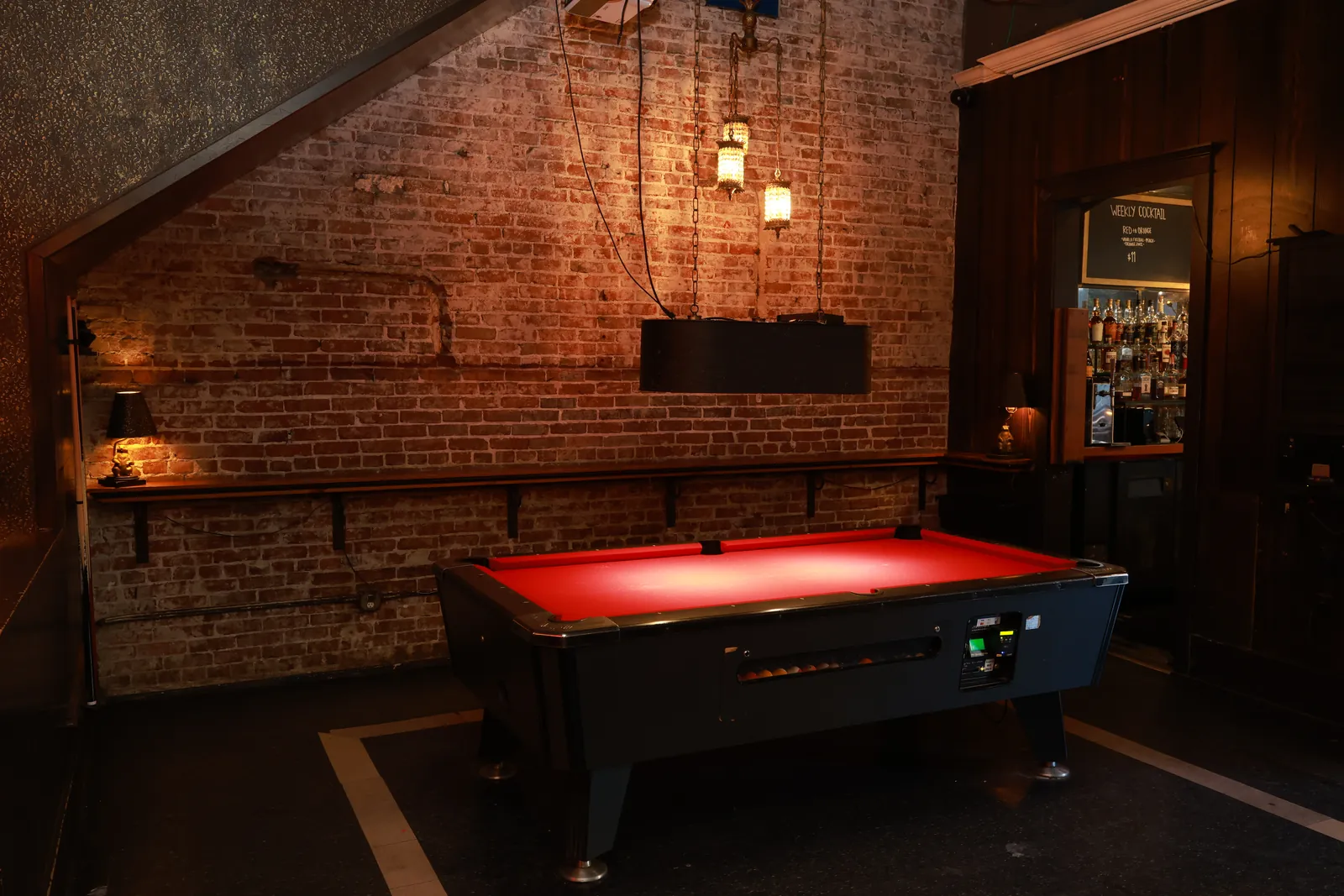 The pool table glowing red under its hanging lamps, brick wall behind